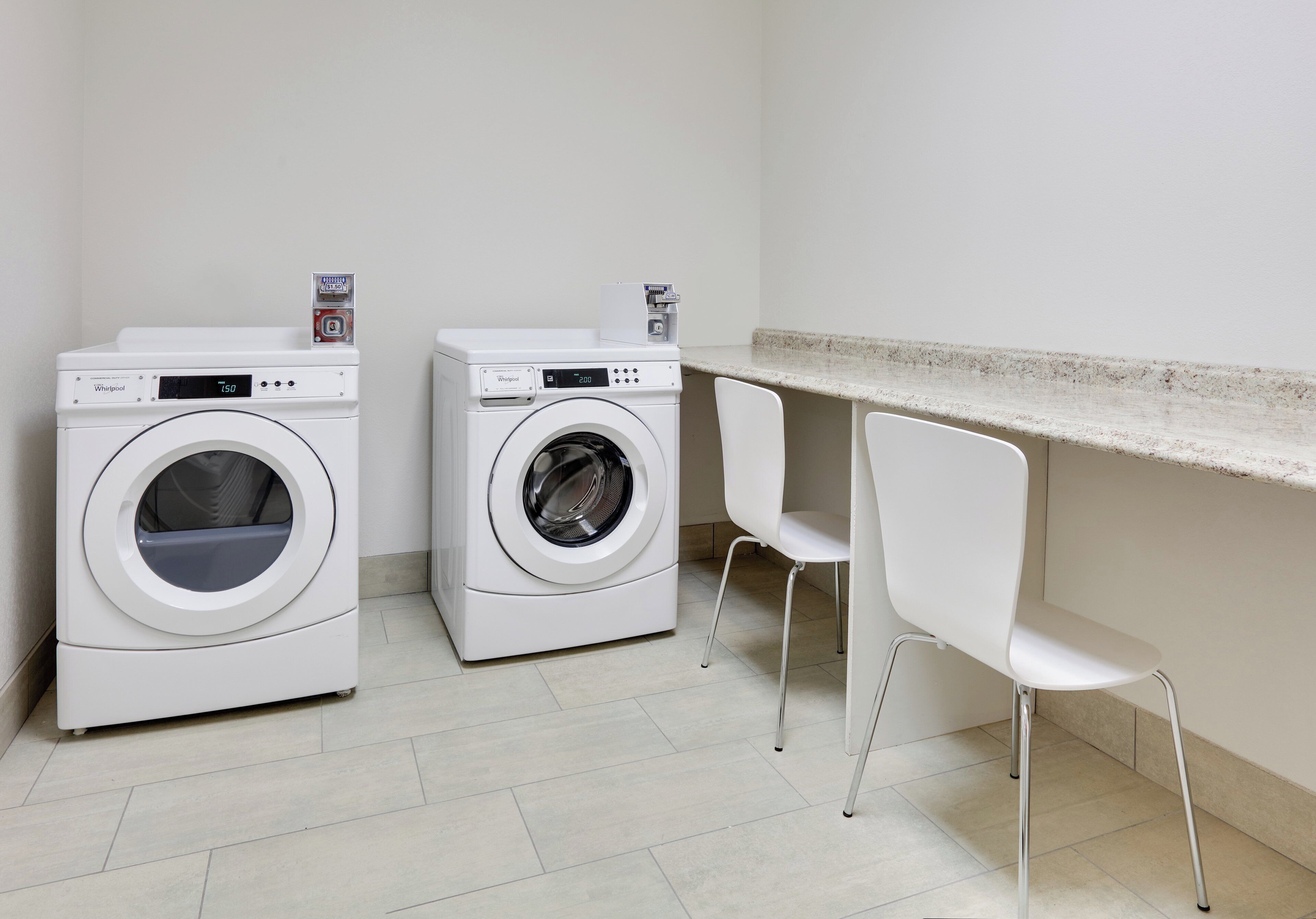 A laundry area with two front-loading washers, a countertop, and two white chairs.