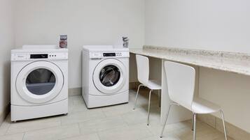 A laundry area with two front-loading washers, a countertop, and two white chairs.