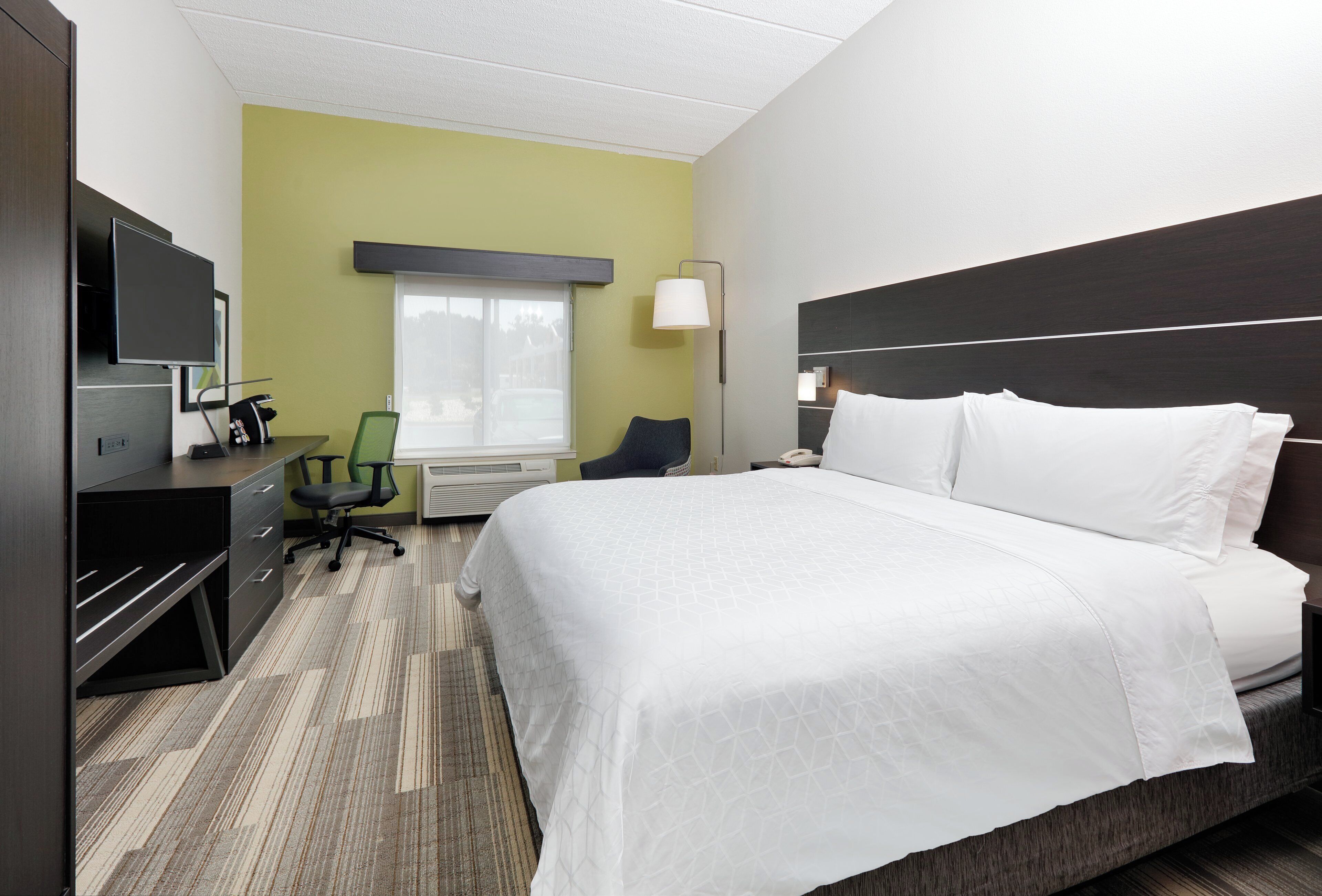 Ein Hotelzimmer mit einem Bett, einem Schreibtisch, einem Stuhl, einem Fernseher und einem Fenster.