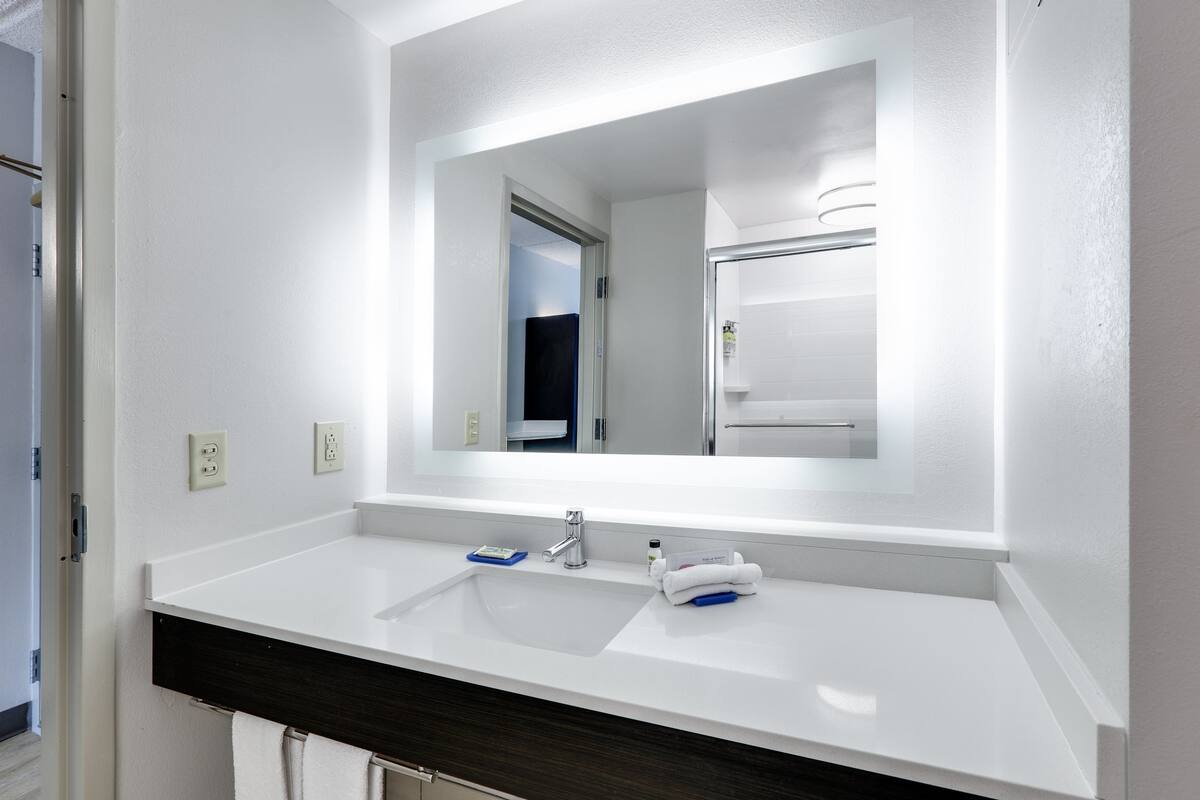 A modern bathroom with a white sink, a large mirror, and a dark wooden vanity.