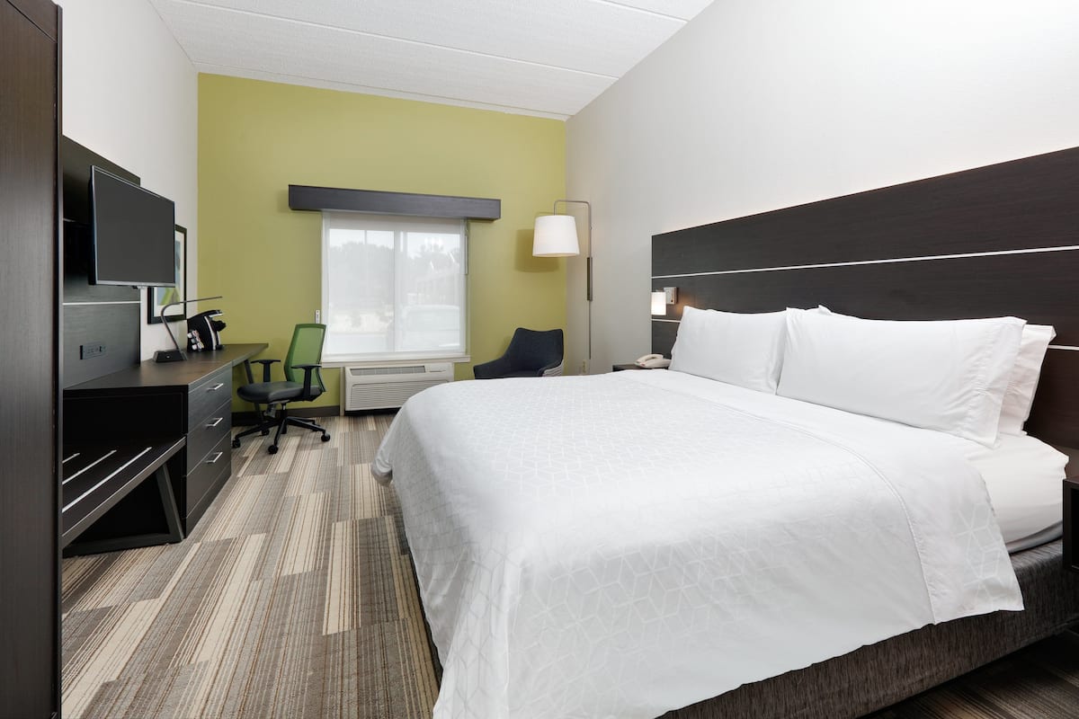 A hotel room with a bed, desk, chair, TV, lamp, and window.