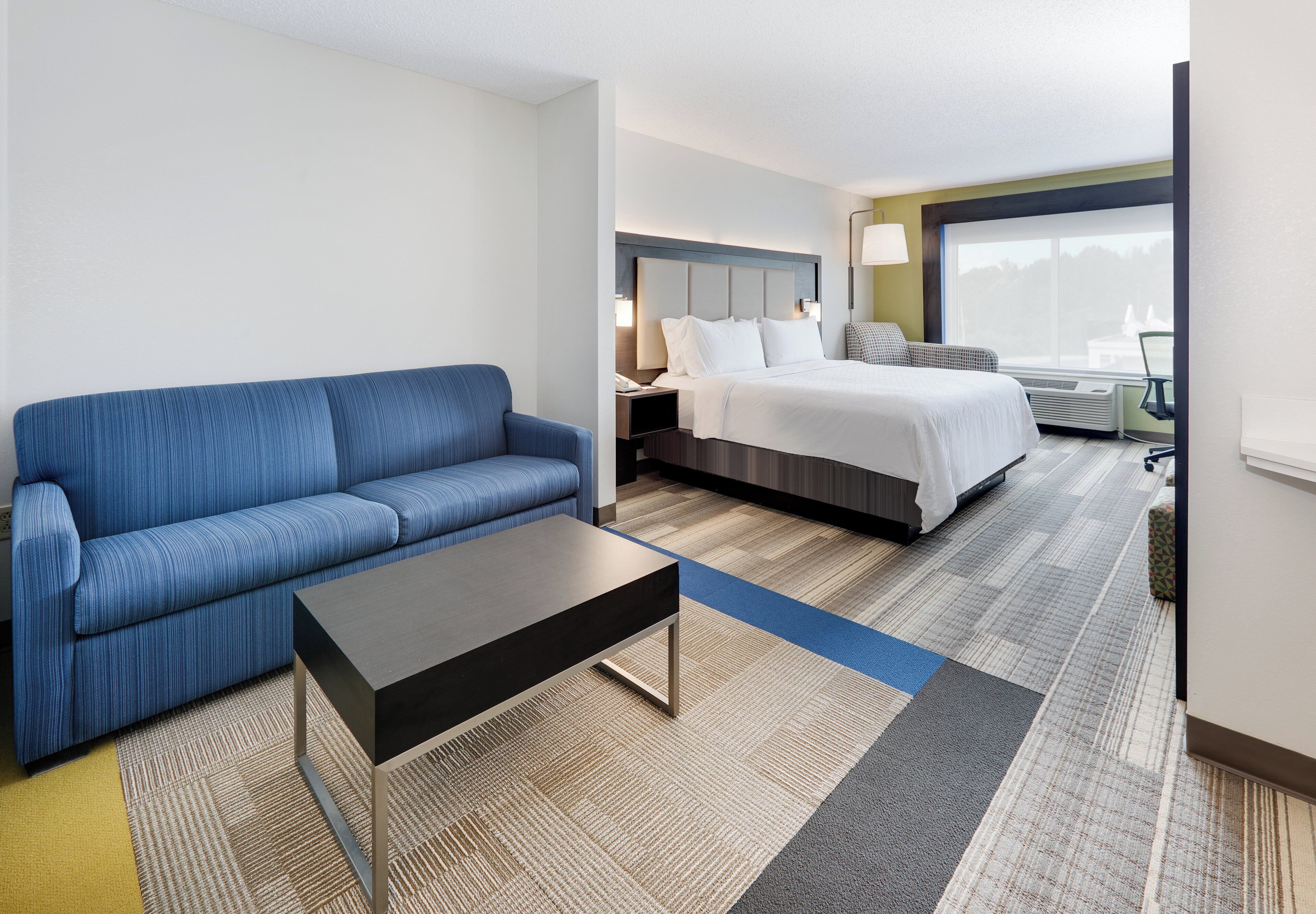 A hotel room with a blue sofa, a bed with white bedding, a small table, and a view of the outdoors.