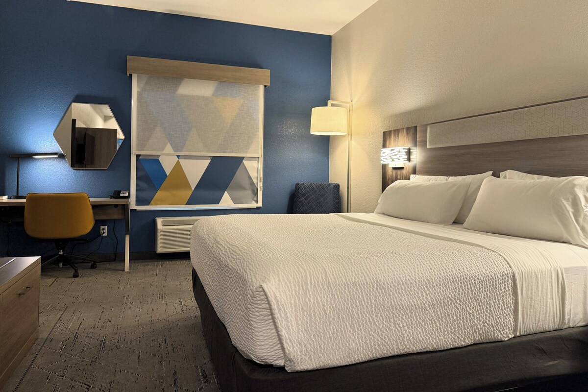 Une chambre d’hôtel comprenant un lit, un bureau, une chaise et une grande fenêtre ornée d’un motif géométrique.
