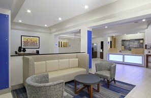 Un lobby moderno con una recepción, un sofá, dos sillones y una pequeña mesa redonda.