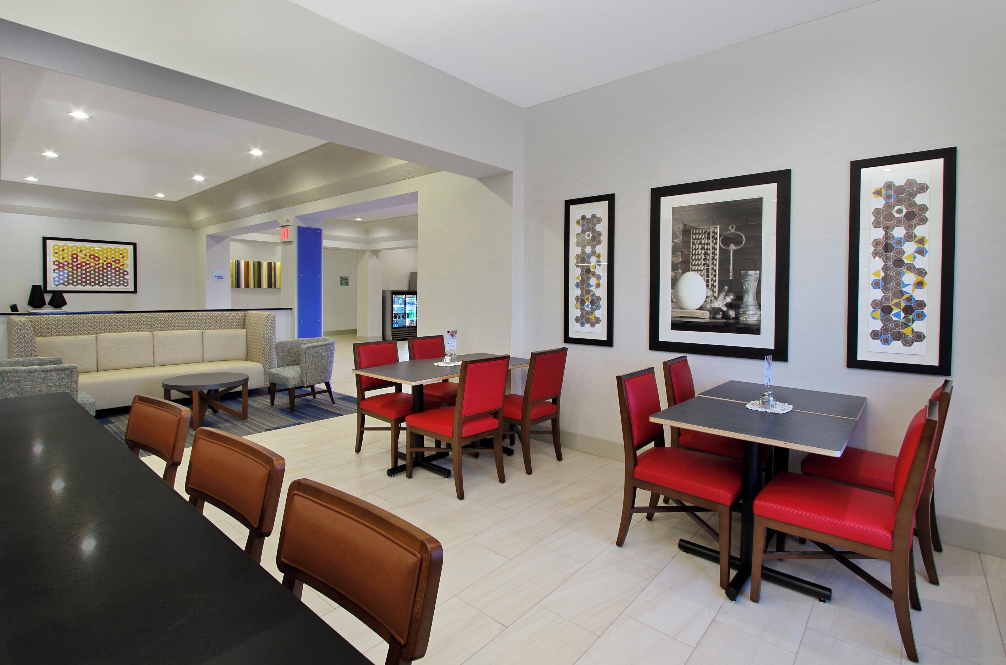 A hotel dining area with red upholstered chairs, a black table, and framed artwork on the walls.