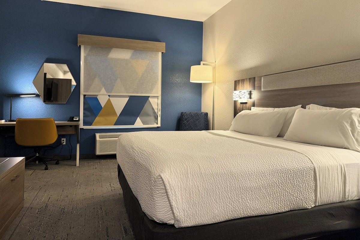 A hotel room with a bed, desk, chair, and a large window with a geometric pattern.