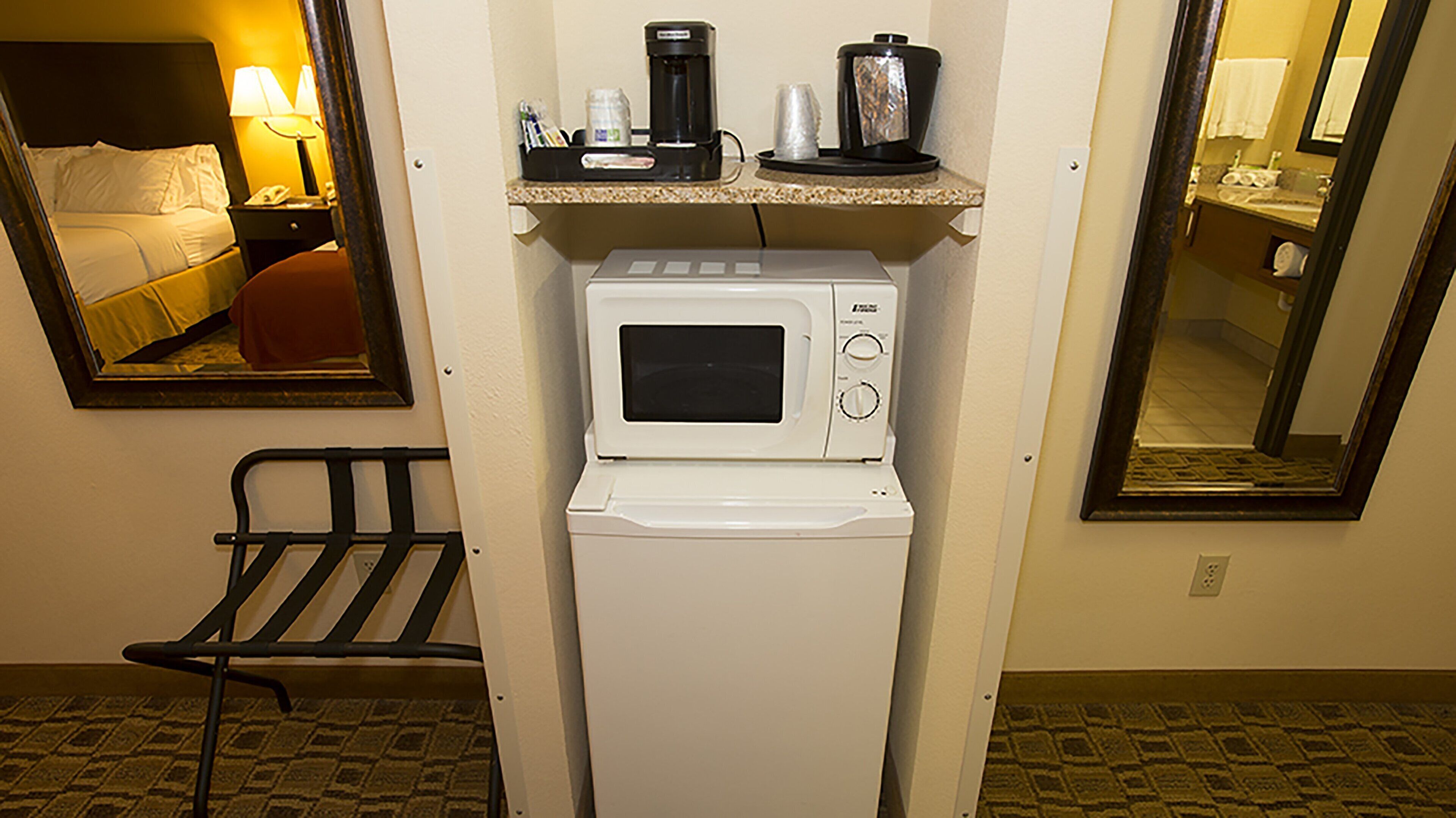 A compact hotel room with a microwave, a coffee maker, and a small seating area.