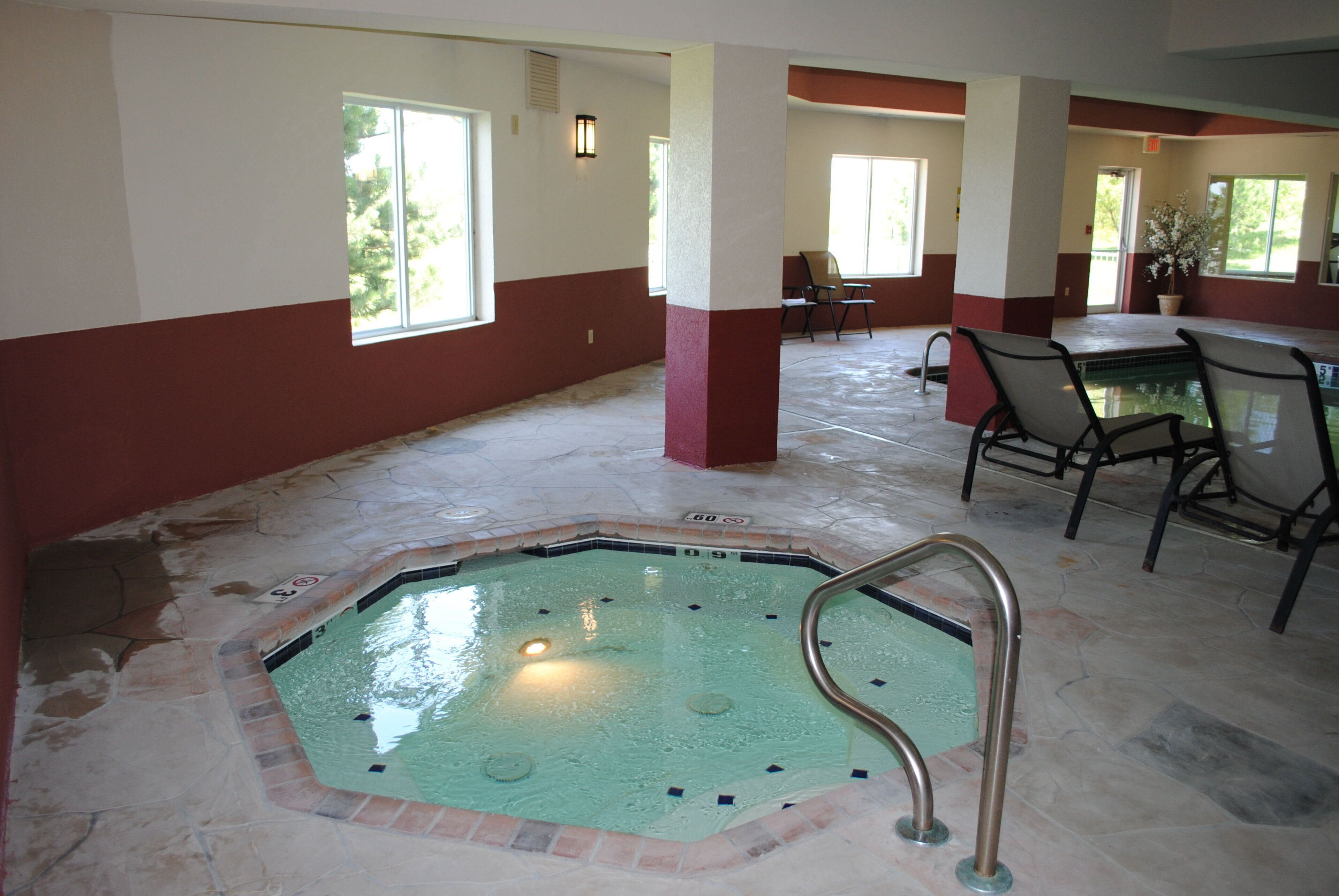 Area piscina con vasca idromassaggio, sedie e pavimento piastrellato.