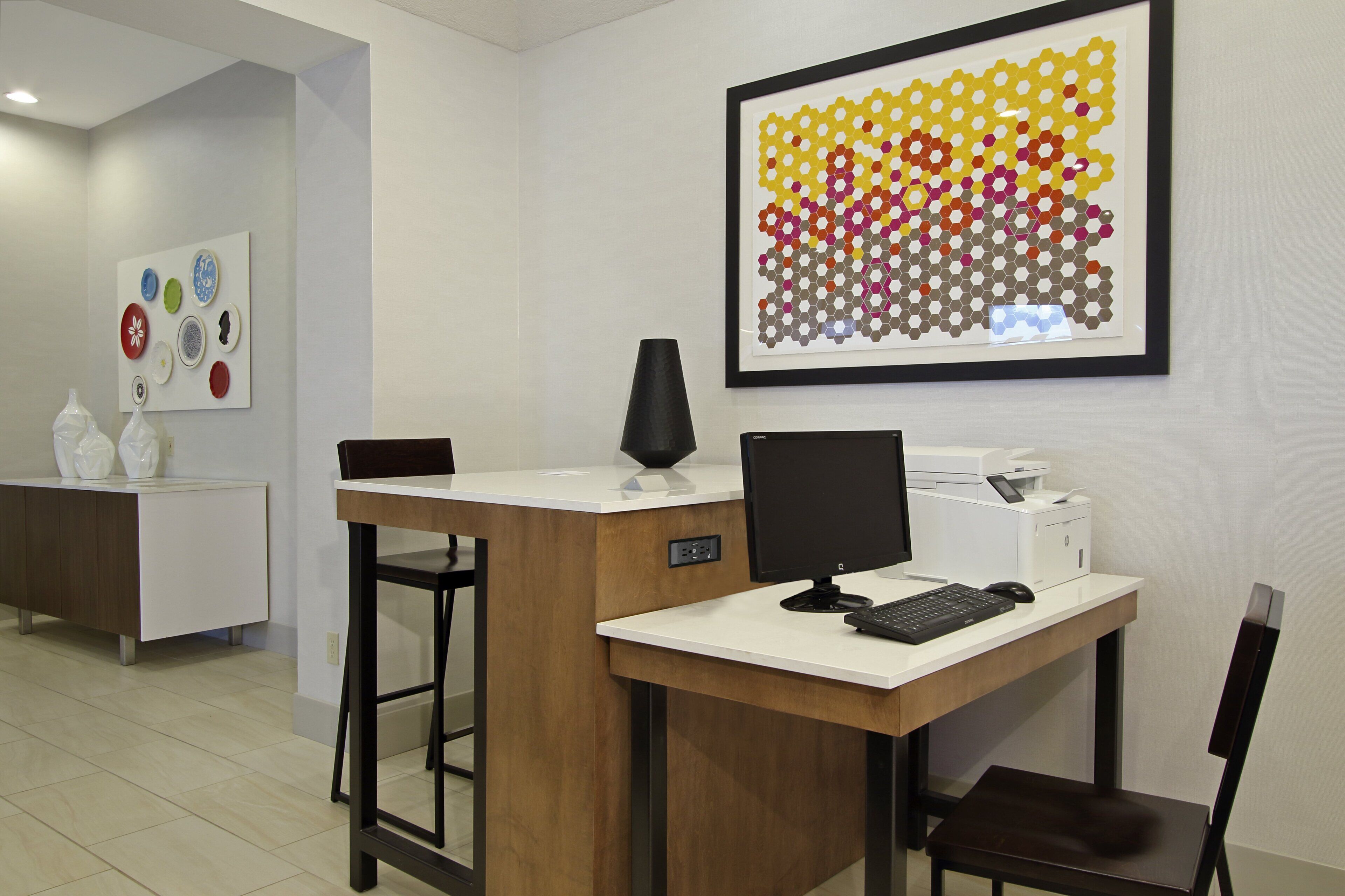 A modern office space with a desk, computer, printer, and a framed abstract art piece on the wall.