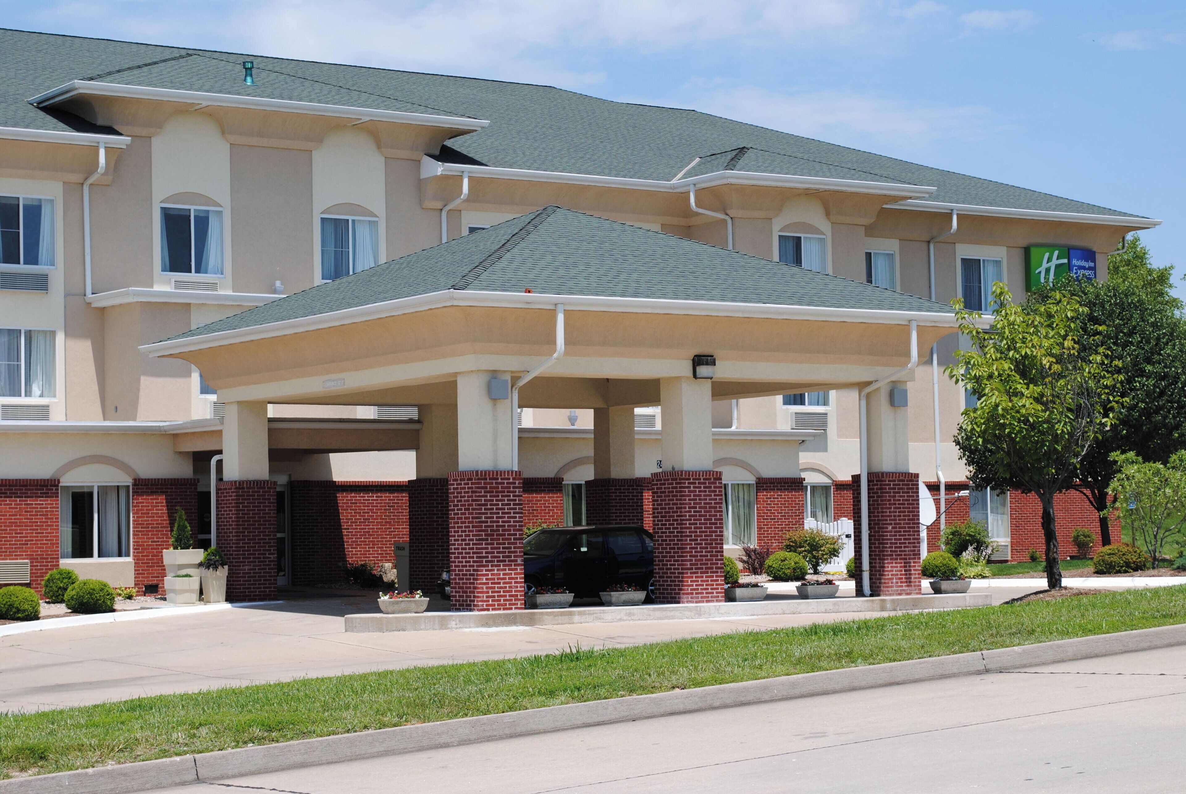 A multi-story hotel with a covered entrance, brick facade, and a parking area with a black SUV.