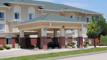 A multi-story hotel with a covered entrance, brick facade, and a parking area with a black SUV.