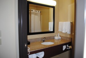 A bathroom with a sink, mirror, towel rack, and a towel dispenser.