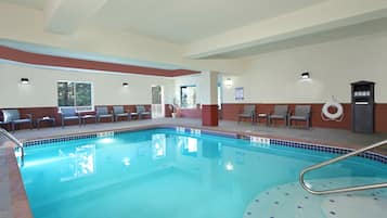 Une piscine intérieure avec un bord carrelé, une bouée de sauvetage et des chaises disposées autour de la piscine.