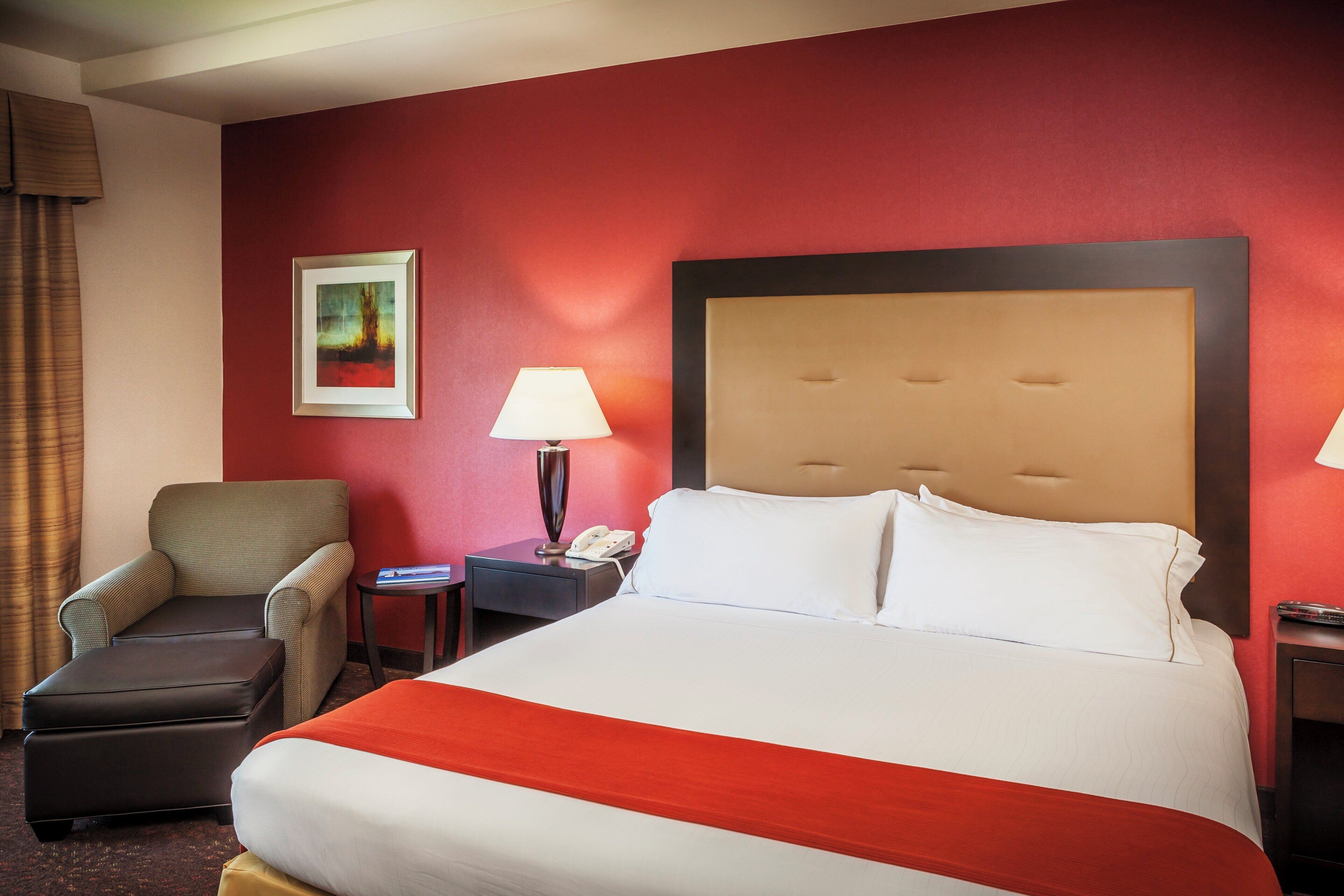 A hotel room with a bed, a chair, a nightstand with a lamp, and a painting on the wall.