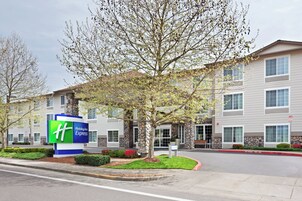 Edificio de Holiday Inn Express con fachada de piedra, un amplio cartel de entrada y una zona de acceso para vehículos en la calle.