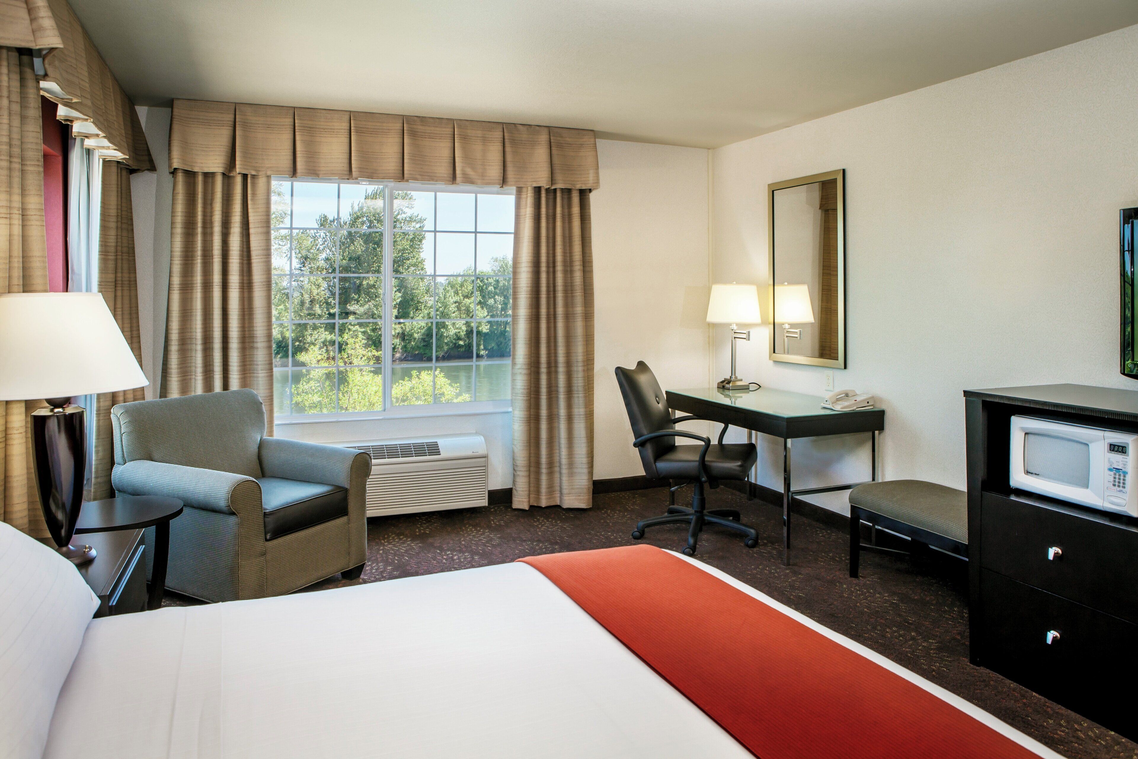 A hotel room with a bed, a desk, a chair, a TV, and a window with curtains.