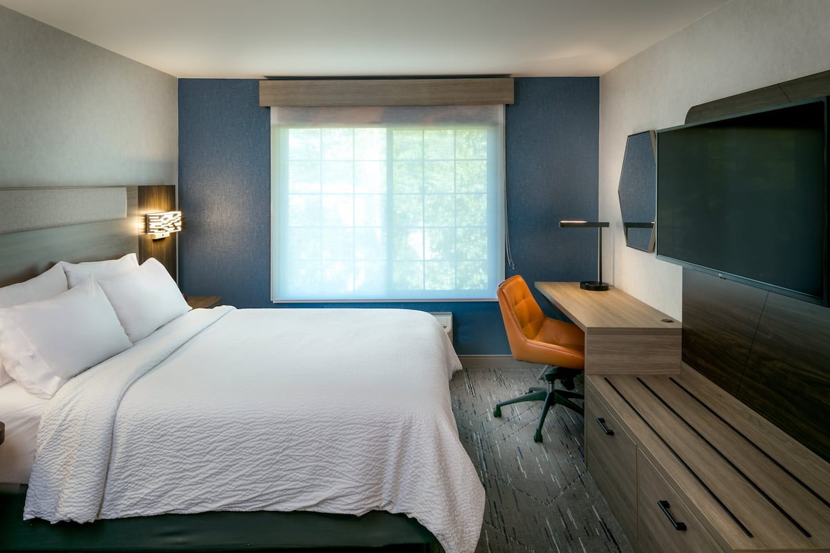 Une chambre d’hôtel équipée d’un lit, d’un bureau, d’une chaise, d’une t élévision et d’une fenêtre avec des stores.
