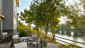 Un patio al aire libre con mesas y sillas, con vista a un cuerpo de agua y árboles.