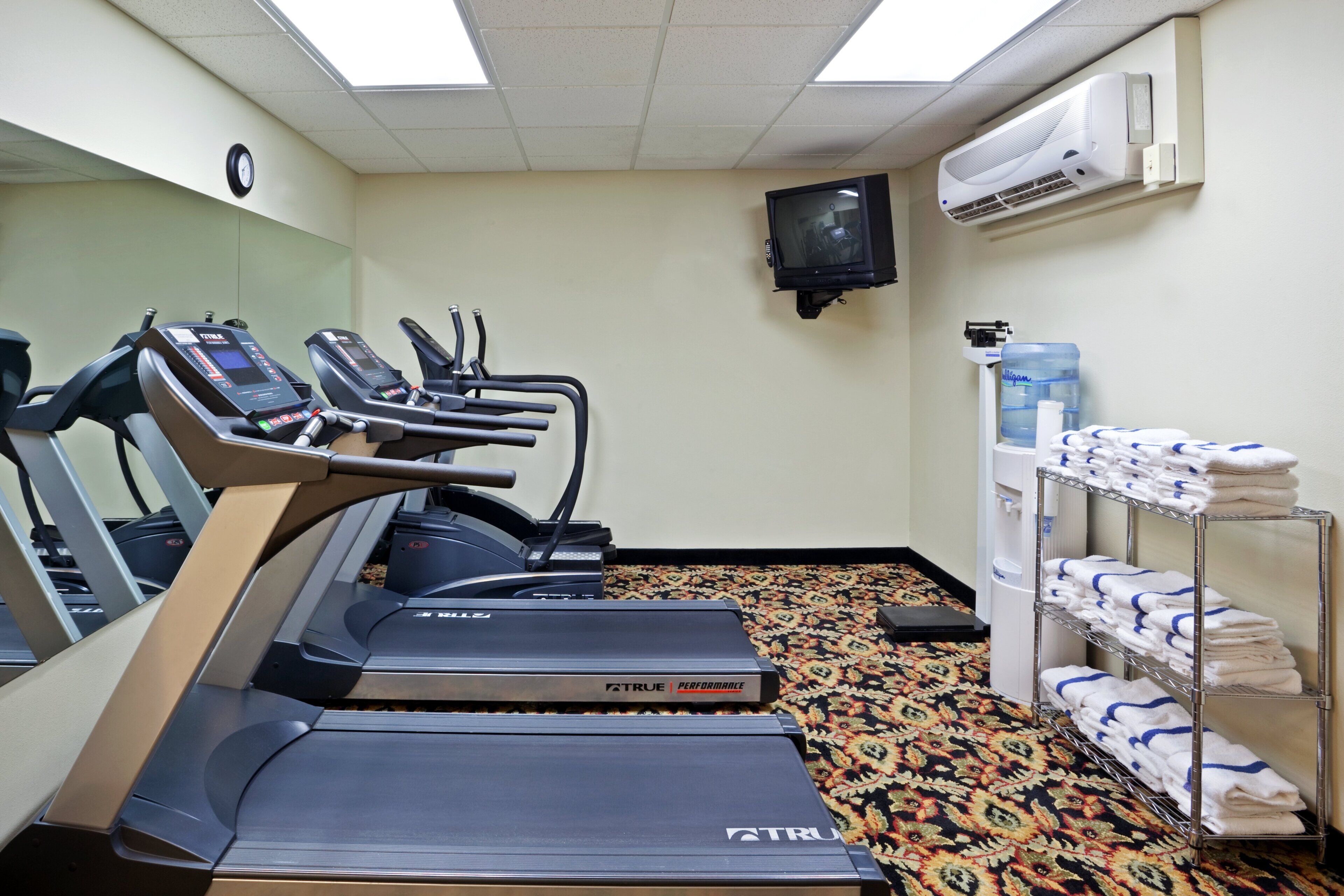 A fitness room with treadmills, a water dispenser, and a towel rack.
