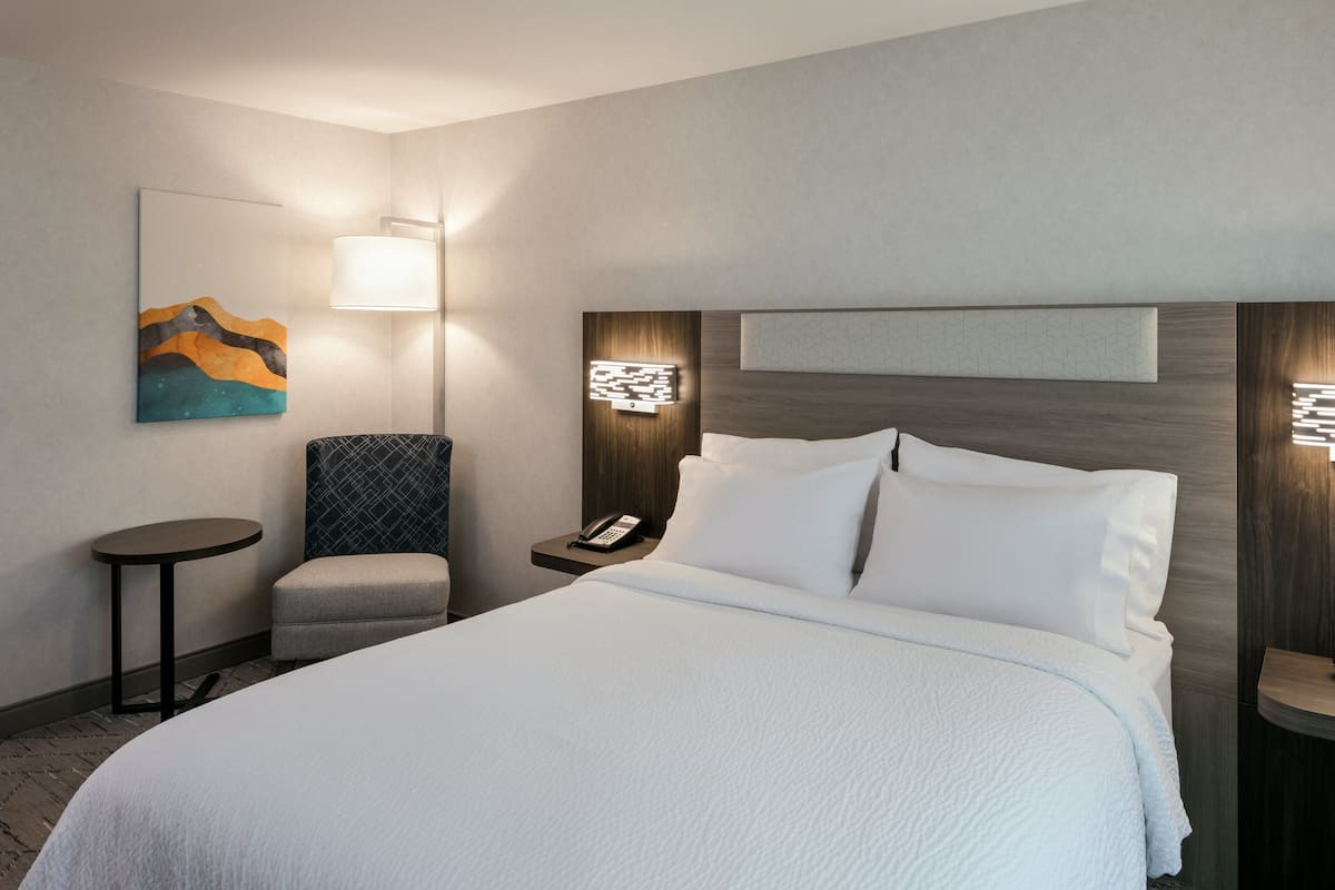 Une chambre d’hôtel avec un grand lit, une chaise, une table de chevet avec un téléphone et une lampe fixée au mur.