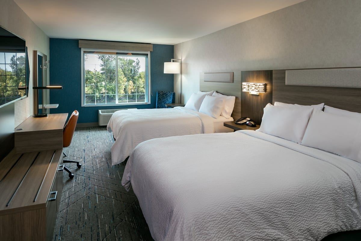 Une chambre d’hôtel avec deux lits, un bureau, une chaise, une fenêtre donnant sur des arbres et une lampe fixée au mur.