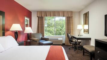 Une chambre d’hôtel avec un lit, deux chaises, un bureau et une grande fenêtre avec des rideaux.