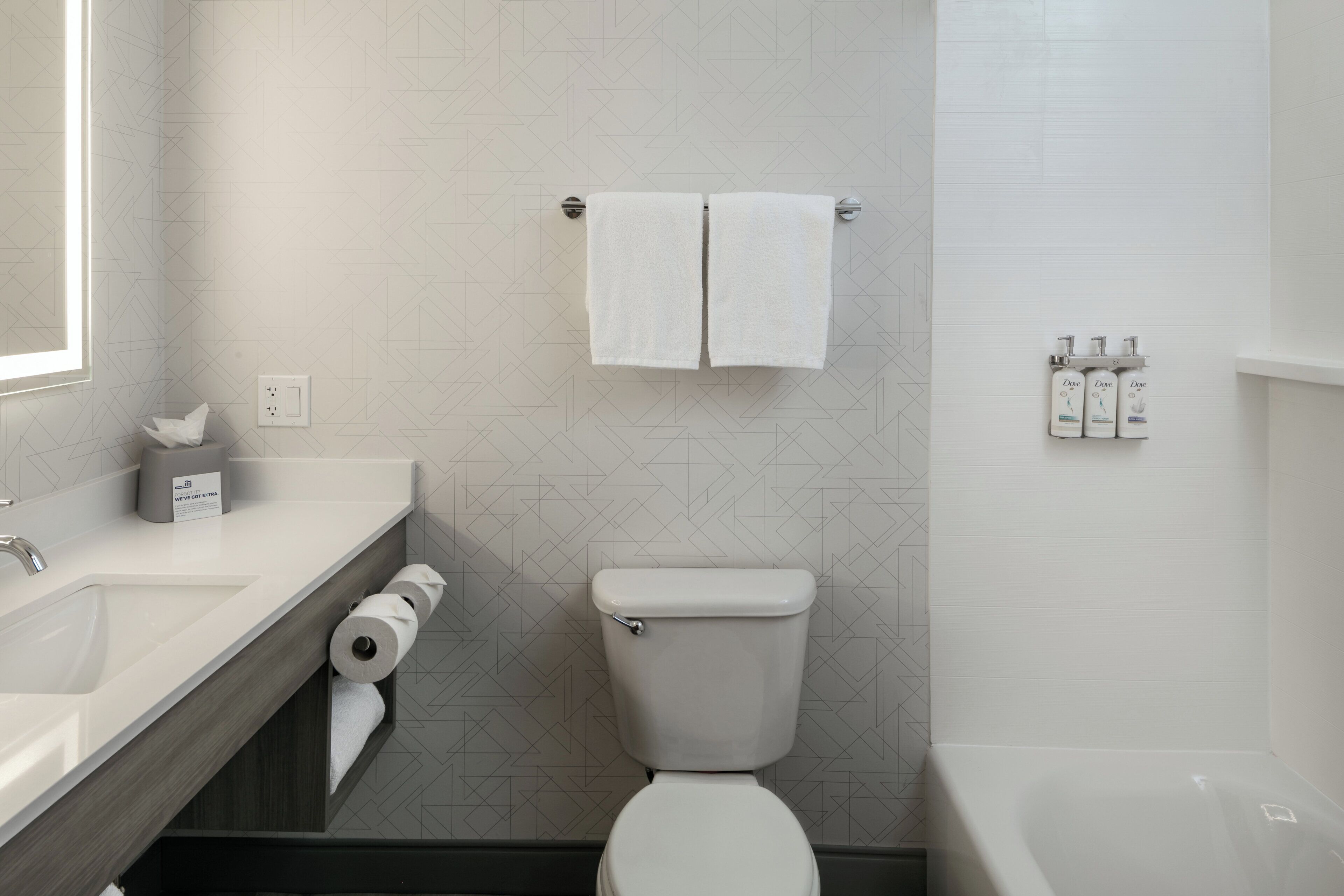 Un baño con inodoro, lavamanos y ducha. Hay toallas colgadas en un tendedero, un soporte para papel higiénico y artículos de tocador en la pared.