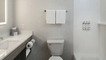 Un baño con inodoro, lavamanos y ducha. Hay toallas colgadas en un tendedero, un soporte para papel higiénico y artículos de tocador en la pared.
