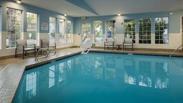 Ein Schwimmbecken mit klarem, blauem Wasser, umgeben von Fenstern und Stühlen.