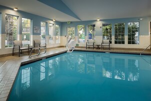 Una piscina con agua azul cristalina, rodeada de ventanas y sillas.