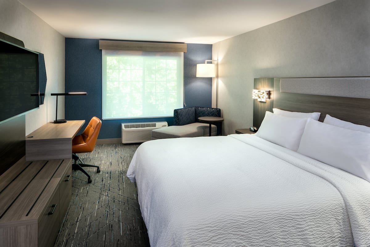 Une chambre d’hôtel avec un grand lit, un bureau, une chaise orange, une petite table et un téléviseur.