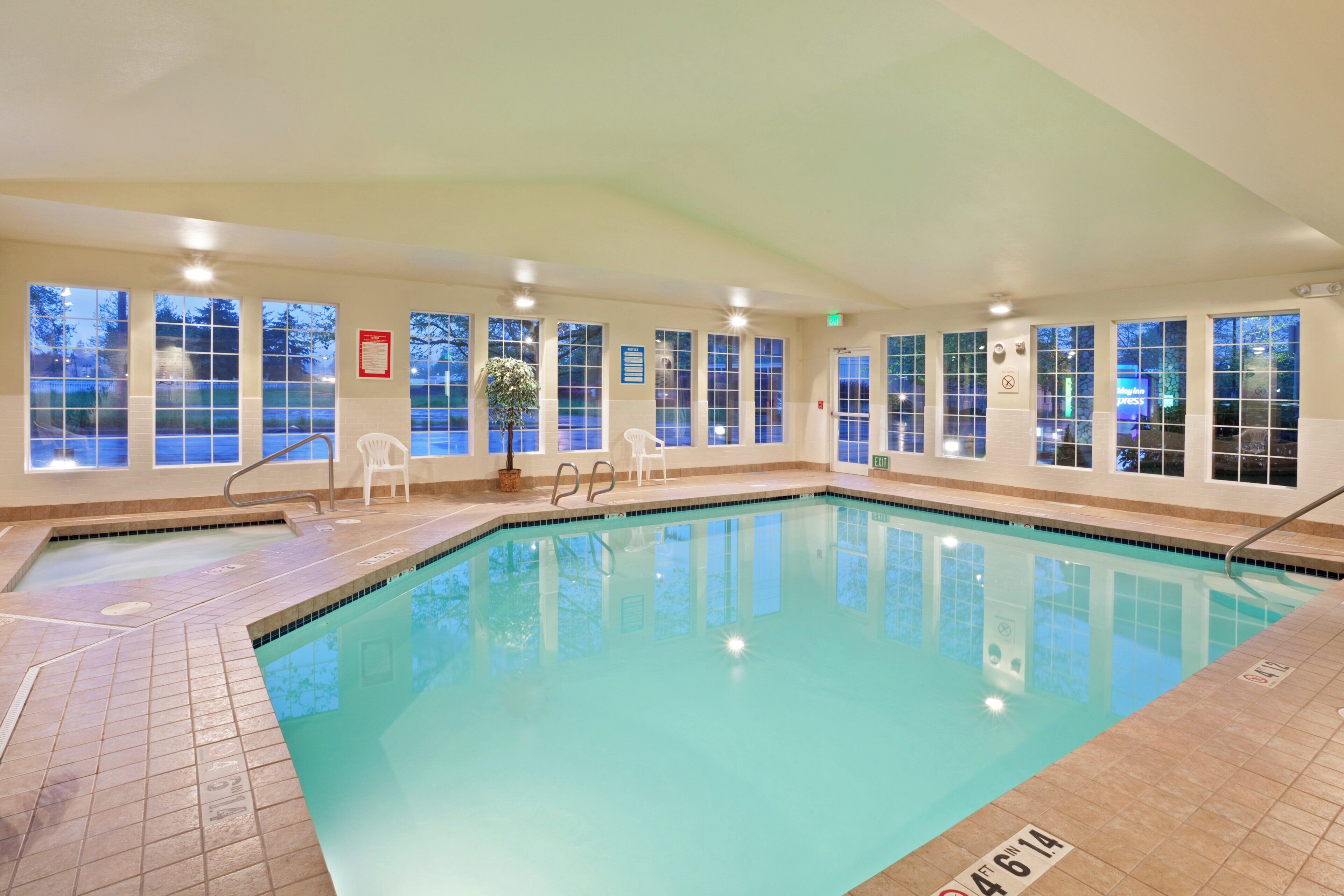 An indoor swimming pool with clear glass walls, multiple exits, and a tiled floor.