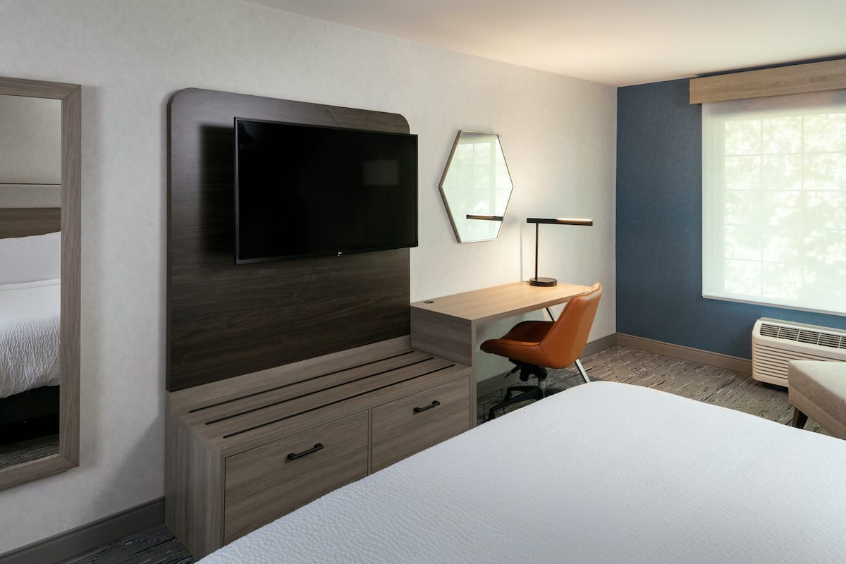 Une chambre d’hôtel avec un lit, un bureau, une chaise, une télévision, un miroir et une fenêtre.