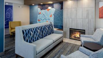 A modern lounge area with a sofa, armchairs, a fireplace, and a patterned wall.