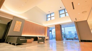 A spacious lobby with a high ceiling, a seating area with sofas and chairs, and large windows allowing natural light.
