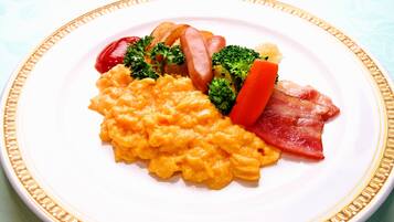 A plate of scrambled eggs, bacon, sausages, and vegetables on a white plate with a gold rim.