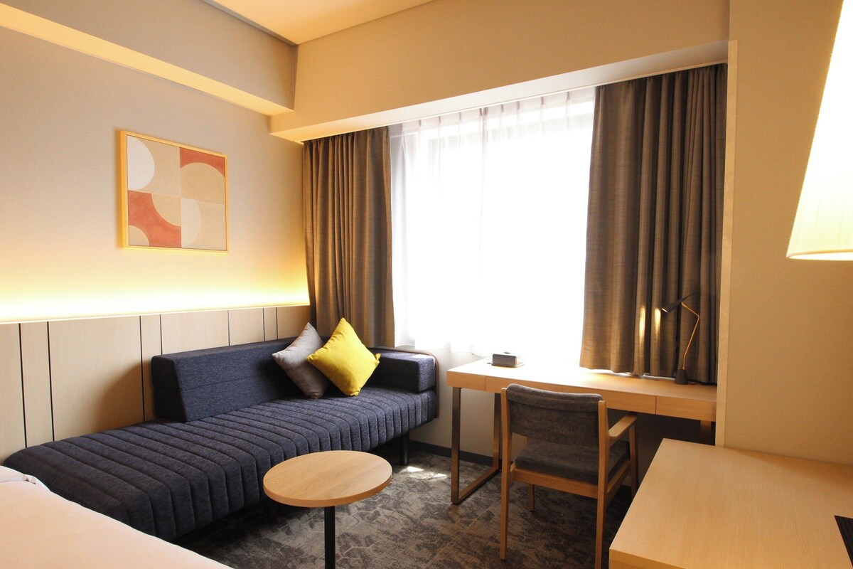 A hotel room with a sofa, a small round table, a desk, and a lamp.