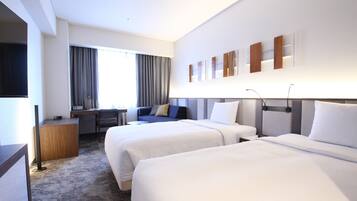 A hotel room with two beds, a desk, a chair, and a TV.