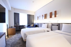 A hotel room with two beds, a desk, a chair, and a TV.