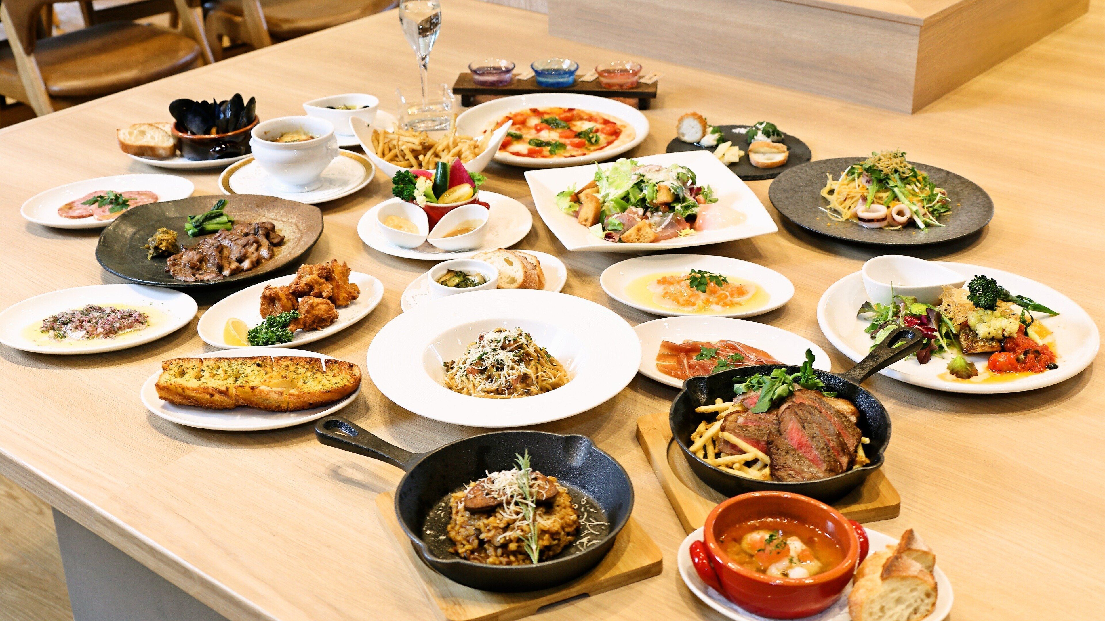 A variety of dishes on a wooden table, including pasta, steak, and salads.