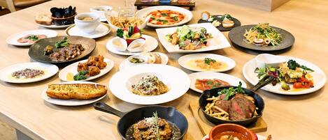 A variety of dishes on a wooden table, including pasta, steak, and salads.