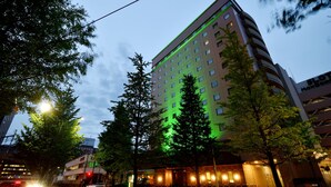 Hotel com vários andares e design moderno, destacando uma entrada imponente e fachada iluminada em verde.