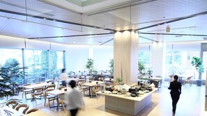 A spacious, modern dining area with high ceilings, large windows, and a central island with food and drinks.