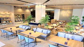 A modern cafe with wooden tables, comfortable seating, and potted plants.