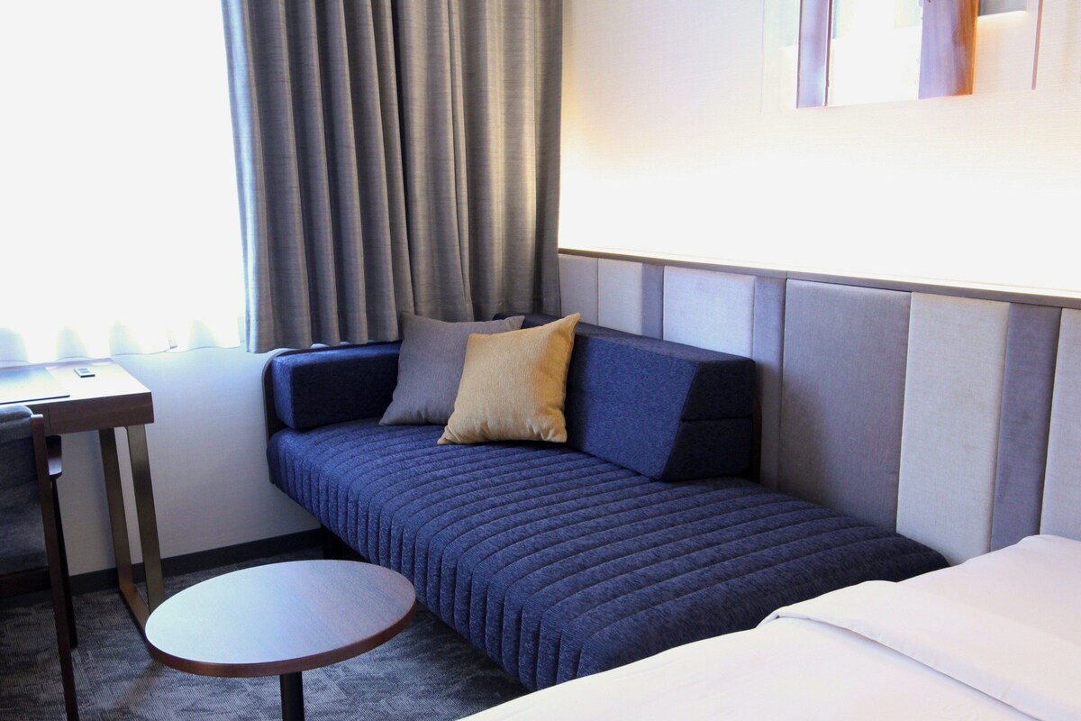 A hotel room with a sofa, a small table, and a bed.