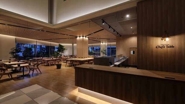 Interior moderno de restaurante com detalhes em madeira, um balcão central e vista para a cidade à noite.