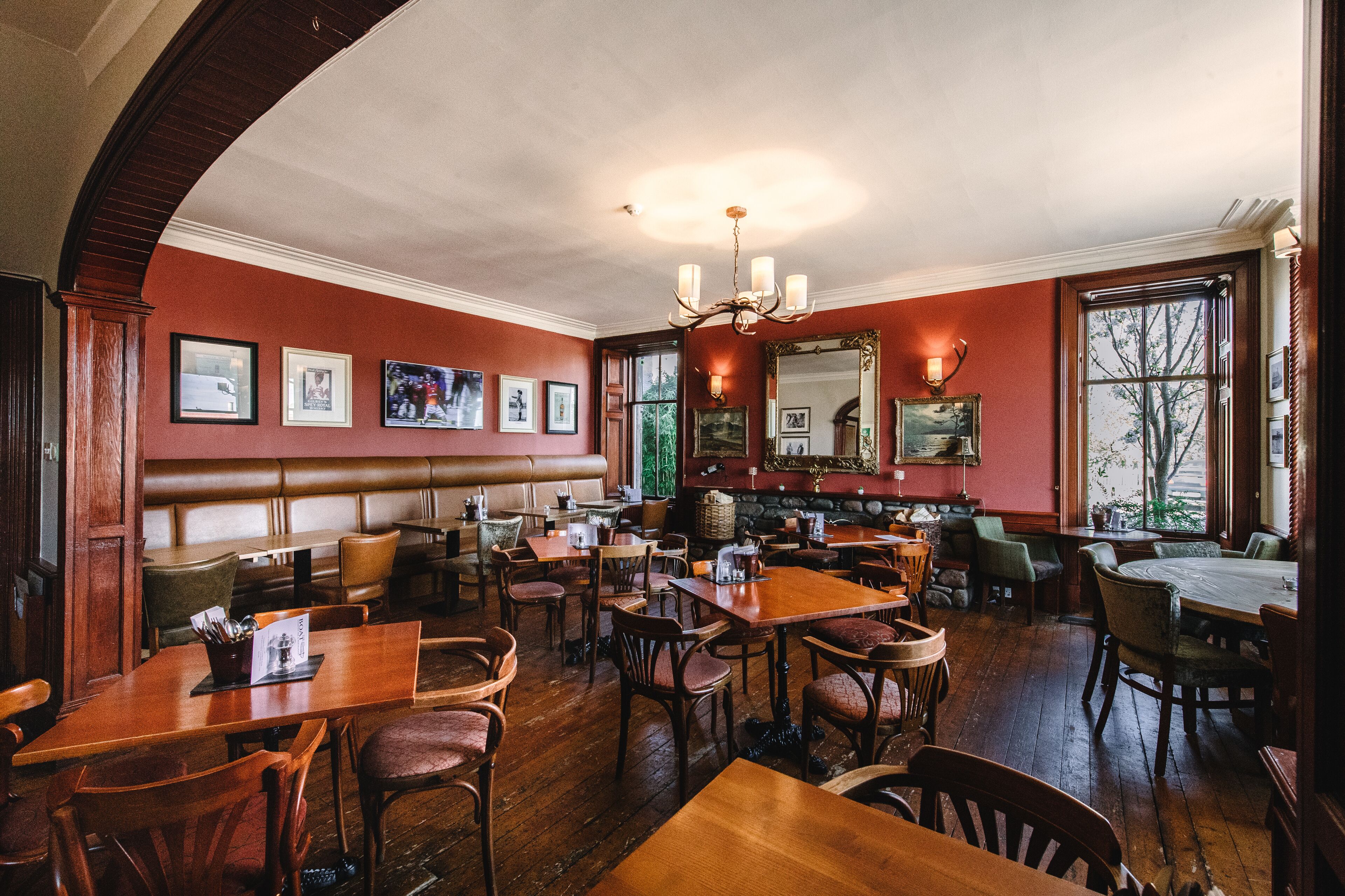 A restaurant with wooden tables and chairs, a chandelier, and framed pictures on the walls.
