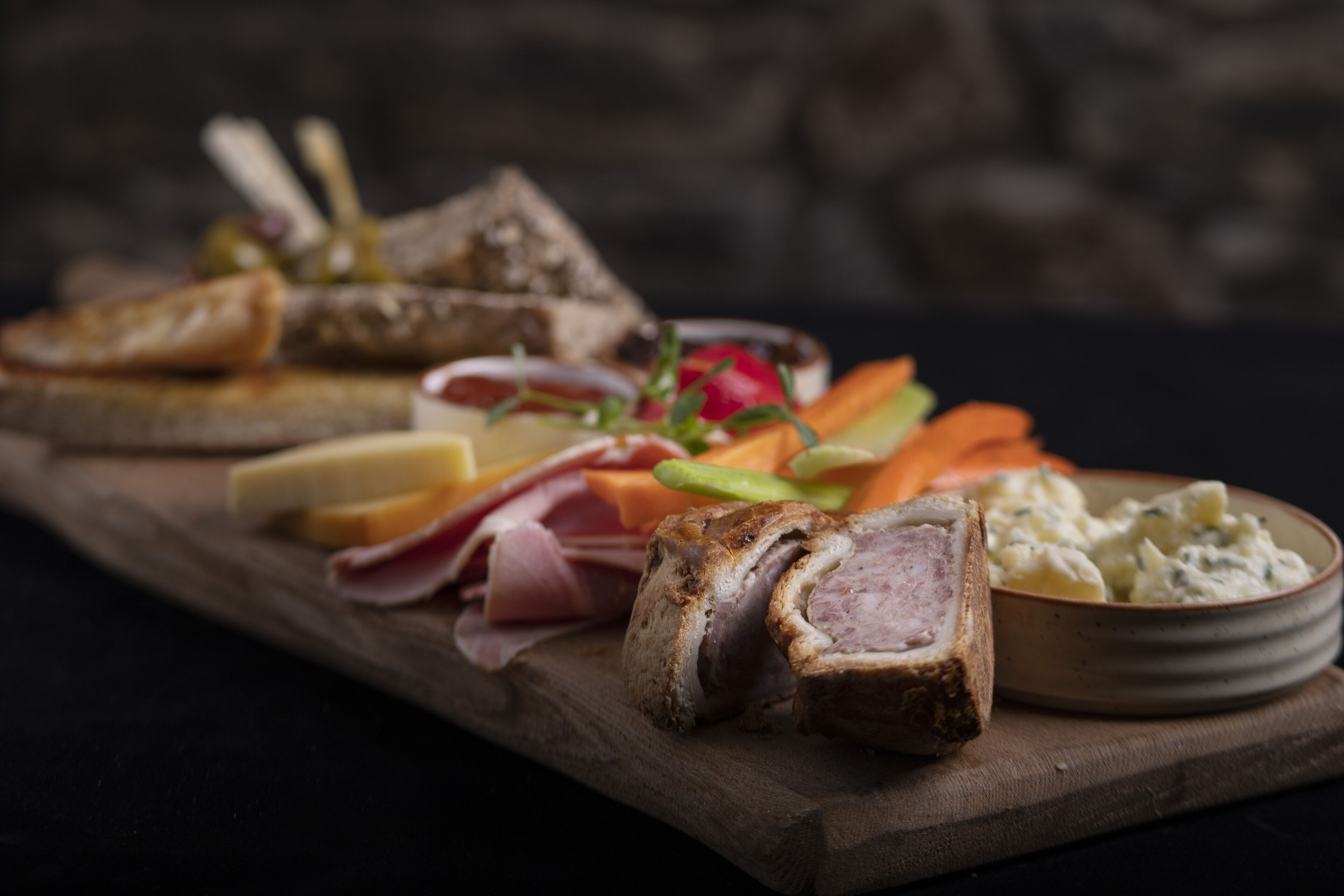 Una tabla de madera con diversos tipos de carne, quesos y verduras.