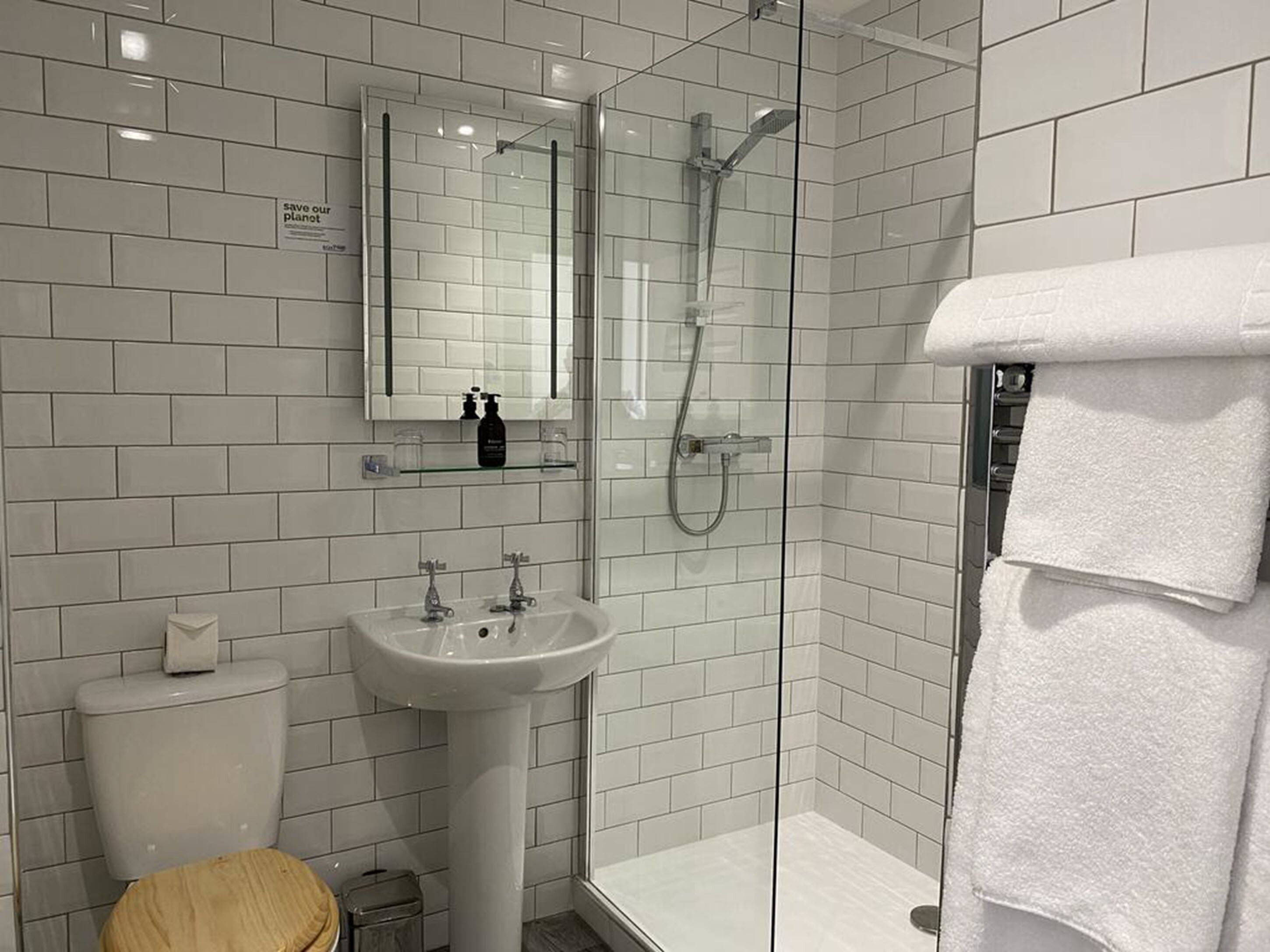 A modern bathroom with white tiles, a glass shower enclosure, a sink, and a toilet.