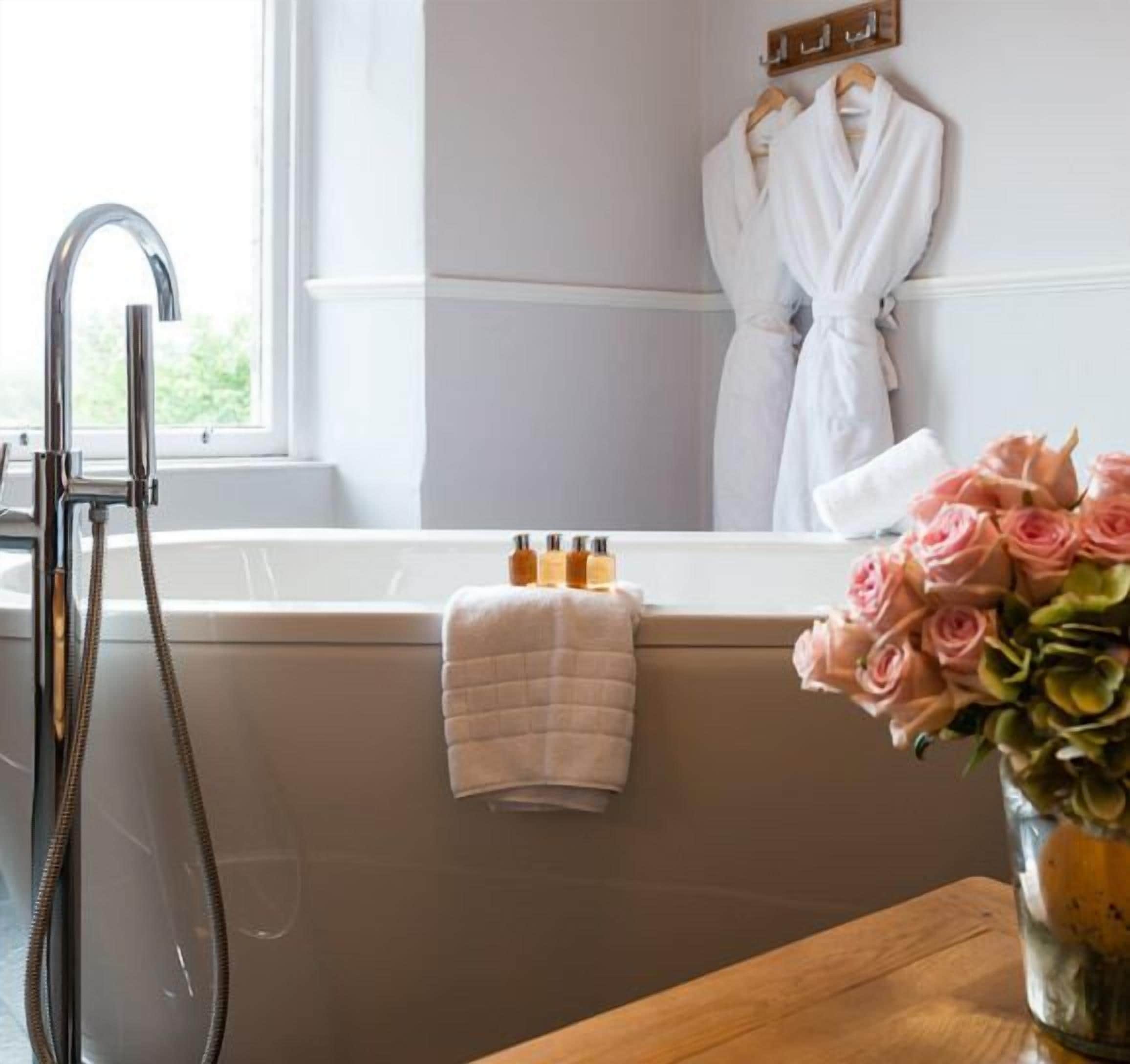 Un baño con bañera, ducha y ventana. Hay una toalla colgada en la pared y un florero con flores en el mostrador.